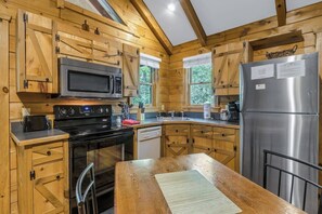 A wooden cabin-style kitchen with a stainless steel refrigerator, microwave, stove, and dishwasher.