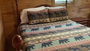 A wooden bed with a patterned quilt and matching pillows, a wooden headboard, and a window with a view of greenery. - My Lakeview Mountain Cabin (Stanardsville)