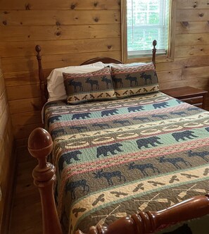 Un lit en bois avec une courtepointe à motifs et des coussins assortis, une tête de lit en bois et une fenêtre donnant sur un paysage verdoyant.