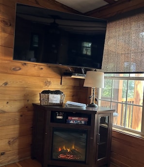A wooden interior with a TV mounted on the wall, a fireplace, and a window with a view.