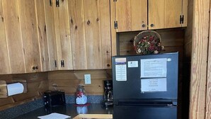 A compact kitchen with wooden cabinets, a black refrigerator, a coffee maker, and a small sink. - My Lakeview Mountain Cabin (Stanardsville)