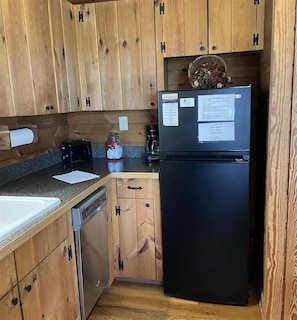 A compact kitchen with wooden cabinets, a black refrigerator, a coffee maker, and a small sink.