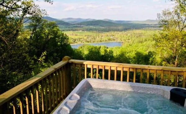 A hot tub on a wooden deck with a view of a lake and mountains.