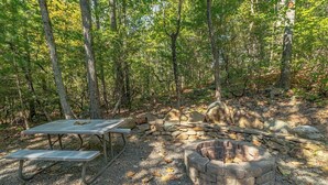 Um camping com um poço de fogueira de pedra, uma mesa de piquenique e um muro de pedra.