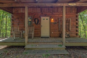 A wooden cabin with a porch, a door, and a bench. - Cabin #7 - Snuggle Den (Stanardsville)