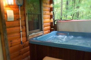 A wooden cabin with a hot tub, a window, and a view of the forest. - Cabin #7 - Snuggle Den (Stanardsville)