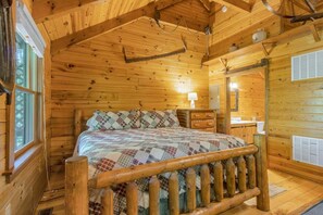 A wooden cabin interior with a bed, a window, a lamp, and a mirror.