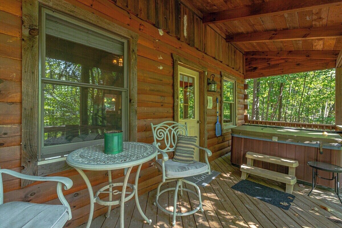 A wooden cabin with a porch, a table with chairs, a bench, and a hot tub.