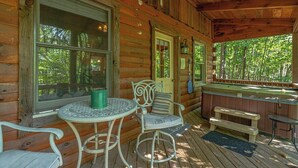Uma cabana de madeira com varanda, mesa e cadeiras, um banco e uma banheira de hidromassagem.