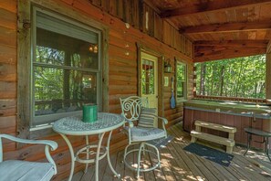 A wooden cabin with a porch, a table with chairs, a bench, and a hot tub.