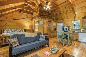 A cozy cabin interior with a sofa, dining table, chairs, a kitchen area, and a ceiling fan.