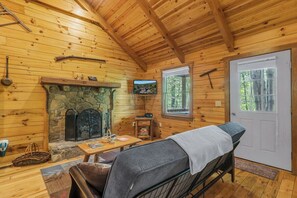 A wooden cabin interior with a stone fireplace, a television, and a door leading outside.