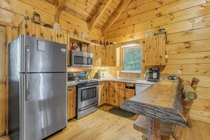 A wooden cabin kitchen with a refrigerator, stove, microwave, and wooden cabinets.