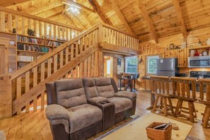 Un interior de madera con sofá, estanterías, una escalera y una zona de cocina.