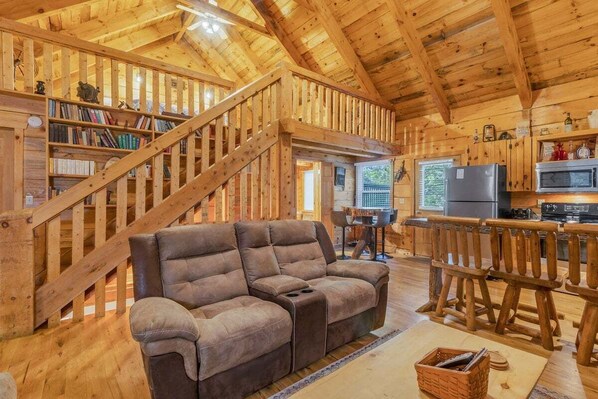 A wooden interior with a sofa, bookshelves, a staircase, and a kitchen area. - Cabin #3 - Honey Pot (Stanardsville)