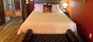 A bed with a headboard, a bedside lamp, and a wooden floor. - Empty Bottle Saloon - Rm. 209 (Stanardsville)