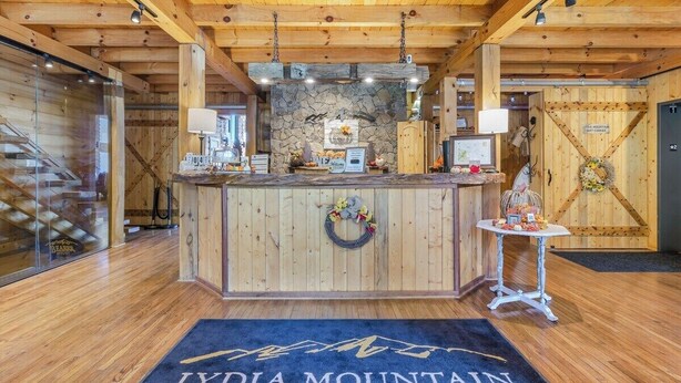 Ein Holzinnenraum mit einer Rezeption, einer Steinwand und einem blauen Teppich mit der Aufschrift 'LYDIA MOUNTAIN'.