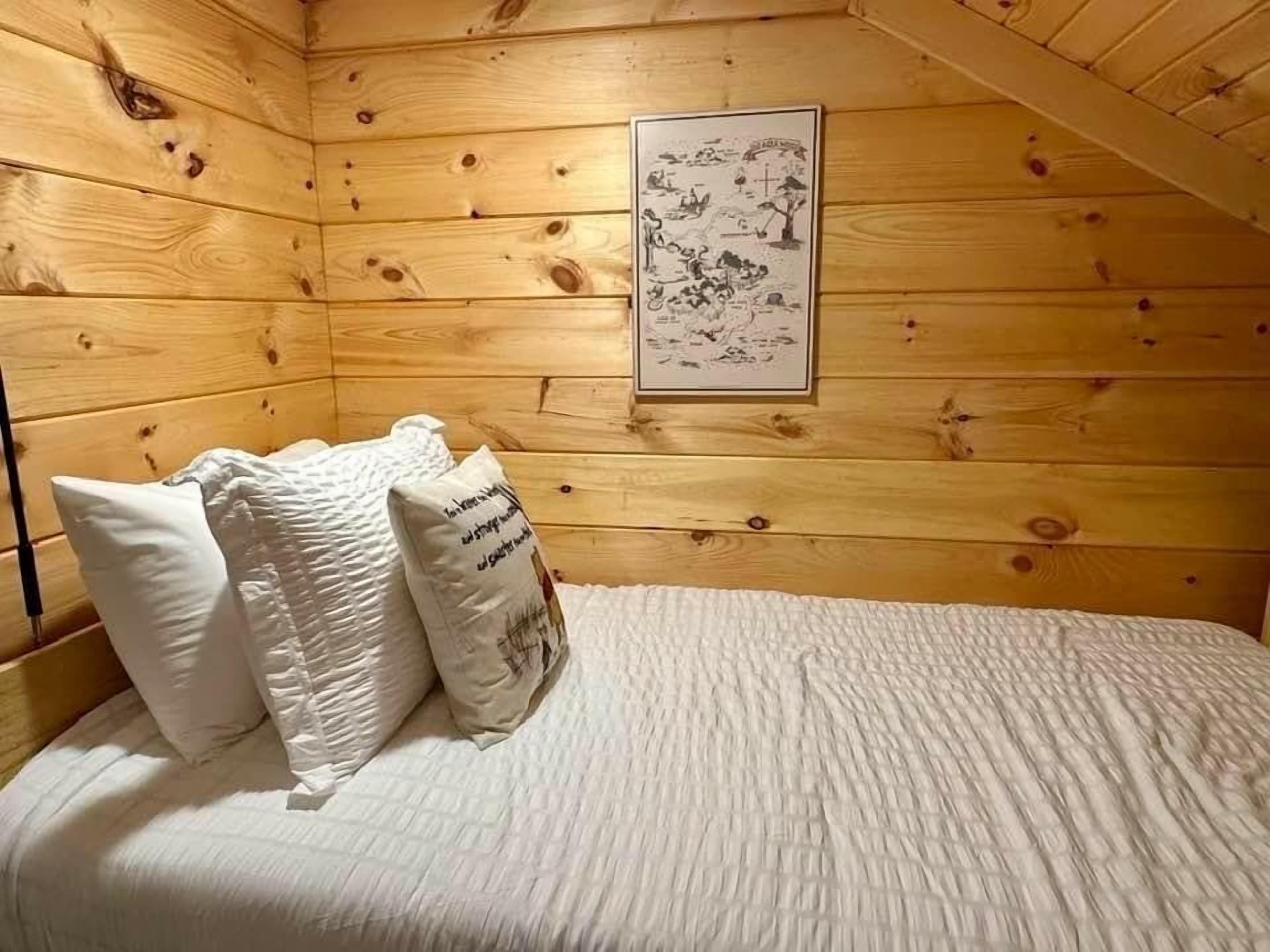 A wooden cabin room with a bed, pillows, and a framed picture on the wall.