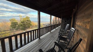 Una terraza de madera con bancos y barandilla, con vista a un paisaje con árboles y una lejana perspectiva.