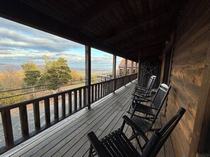 Una terraza de madera con bancos y barandilla, con vista a un paisaje con árboles y una lejana perspectiva.