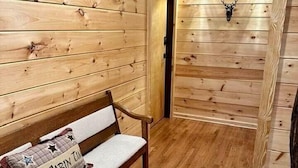 Interior de una cabaña de madera con un banco, una puerta y luces en la pared.