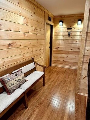 Interior de una cabaña de madera con un banco, una puerta y luces en la pared.