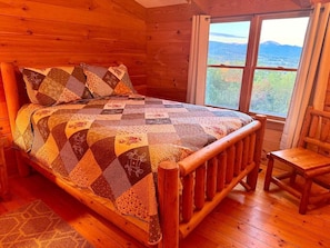 Une chambre dans une cabane en bois, avec un grand lit, une chaise en bois et une fenêtre donnant sur la montagne.