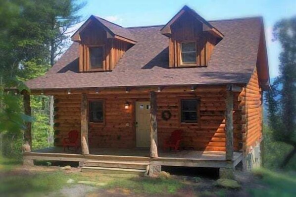 Une cabane en rondins avec un porche, deux fenêtres et une porte.