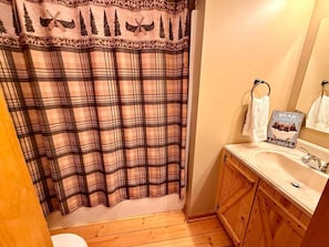 Une salle de bain avec un rideau de douche à carreaux, des meubles en bois, un lavabo et un miroir.