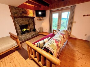 A cozy room with a stone fireplace, a television, a sofa, and a view through a glass door.