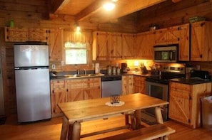 A wooden cabin-style kitchen with a refrigerator, stove, microwave, and wooden cabinets. - The Crooked Oak Cabin (Stanardsville)