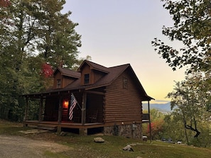 A rustic log cabin with a porch, a flag, and a view of the mountains.