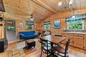 L’intérieur d’un chalet en bois comprend une table à manger, des chaises, un canapé, une cheminée et un coin cuisine.