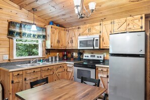 Una cocina estilo cabaña con armarios de madera, un refrigerador de acero inoxidable, un microondas, una estufa y una mesa de comedor.