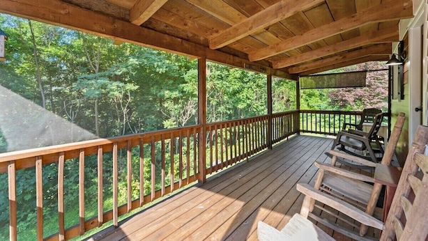 Une terrasse en bois avec une rambarde, des chaises et une vue sur une forêt.