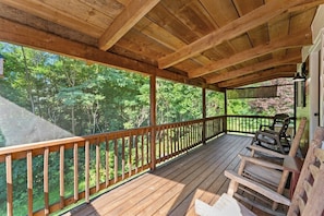 Une terrasse en bois avec une rambarde, des chaises et une vue sur une forêt.