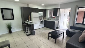 A modern living room with a sofa, coffee table, and a dining area with a kitchen in the background. - Cozy apartment in Hollywood. Ideal Location Near Beach, Shops, and Highways (Hollywood)