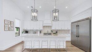 A modern kitchen with white cabinets, a stainless steel refrigerator, and a central island with bar stools. - High Cotton: Private beach steps away, Heated pool, Brand new luxury home (Miramar Beach)
