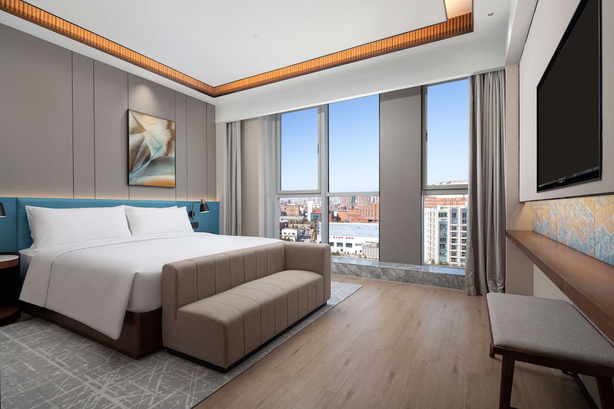 Una habitación de hotel moderna con una cama grande, un área de descanso, un televisor y vistas a la ciudad.