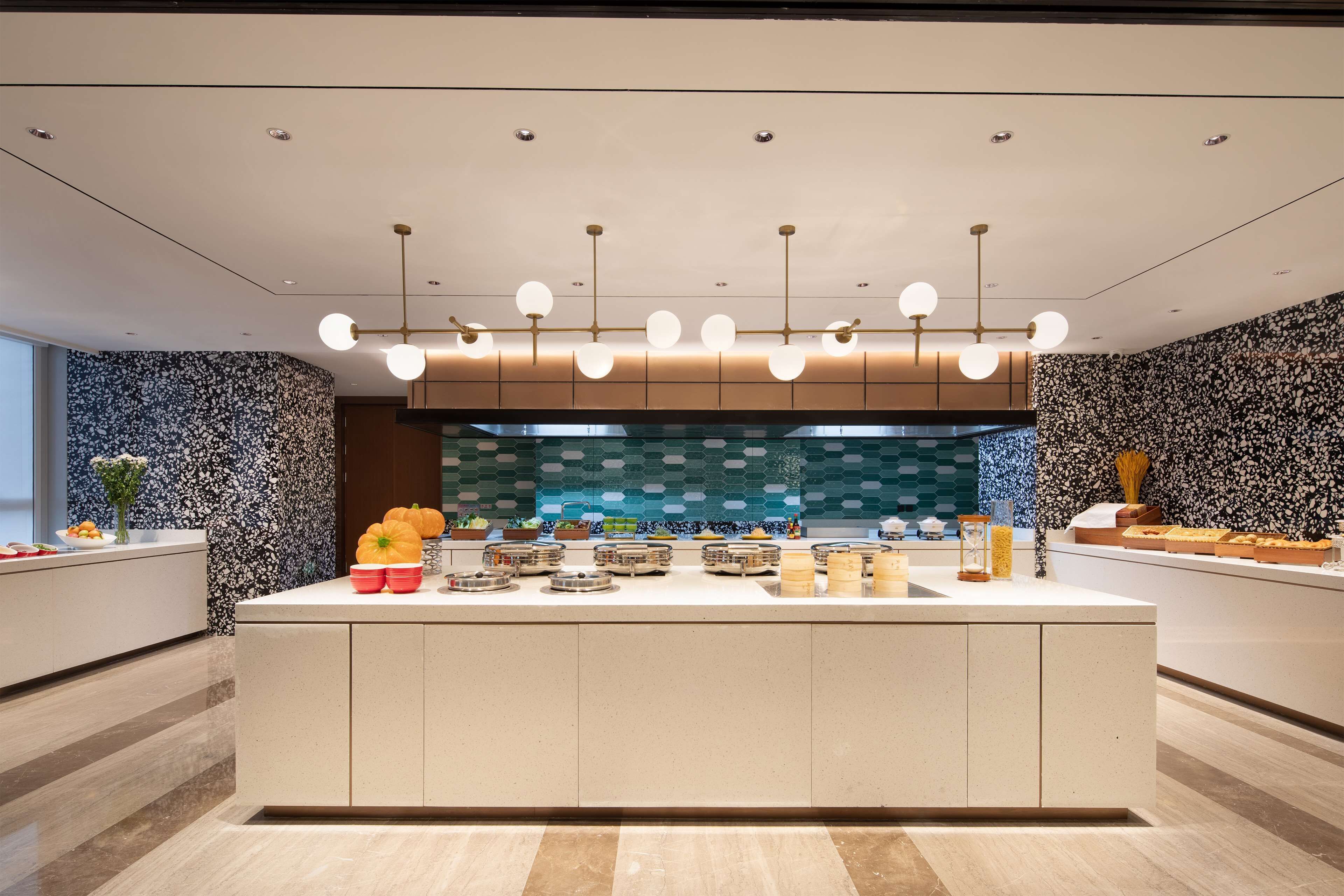 Une cuisine moderne dotée d’un îlot central, de luminaires suspendus et d’un revêtement mural décoratif.