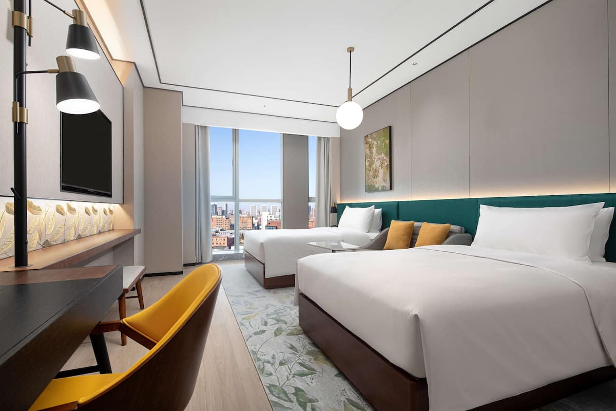 Habitación de hotel con una cama grande, dos camas más pequeñas, un escritorio con silla, televisión y vistas a la ciudad.