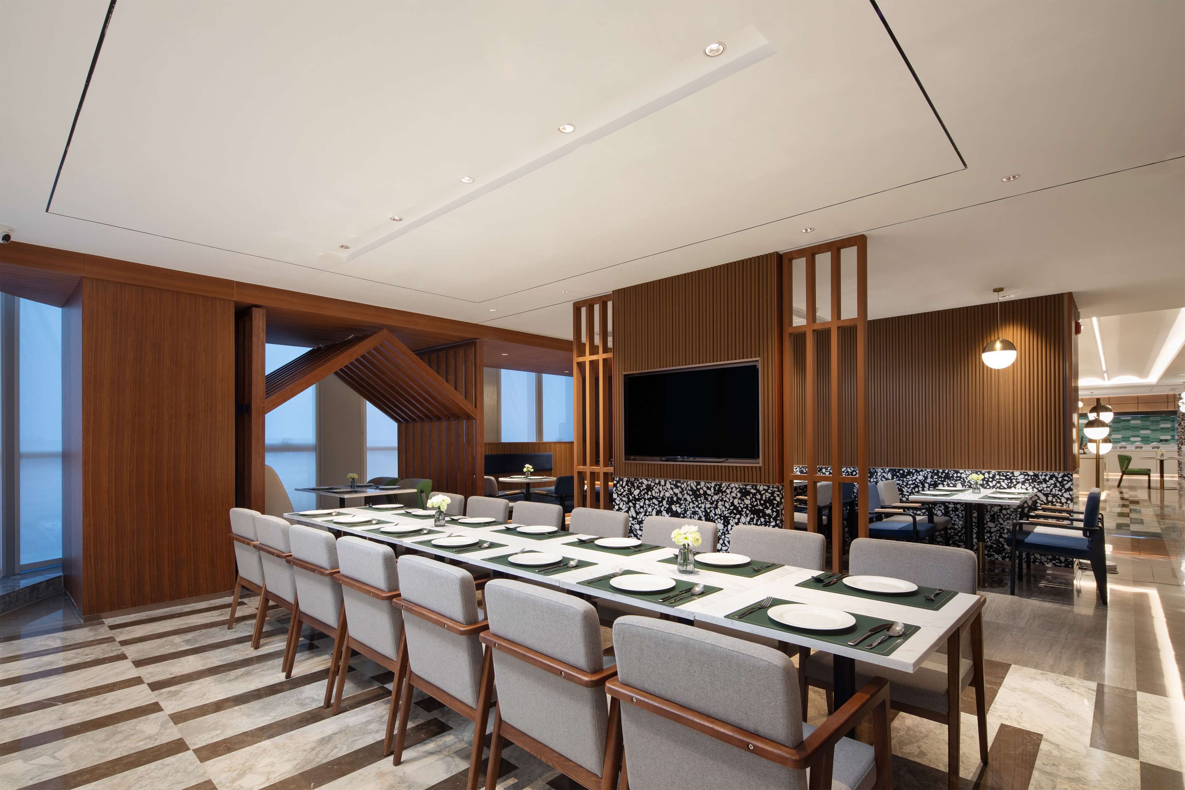A modern conference room with a long table set for a meeting, equipped with a large flat-screen TV and wooden paneling.