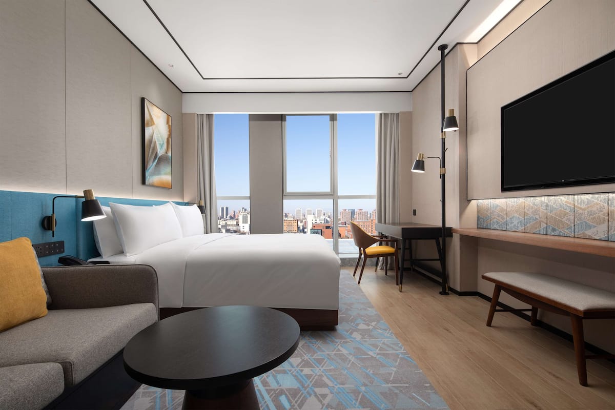 Una habitación de hotel moderna con una cama grande, un sofá, un escritorio y un televisor.