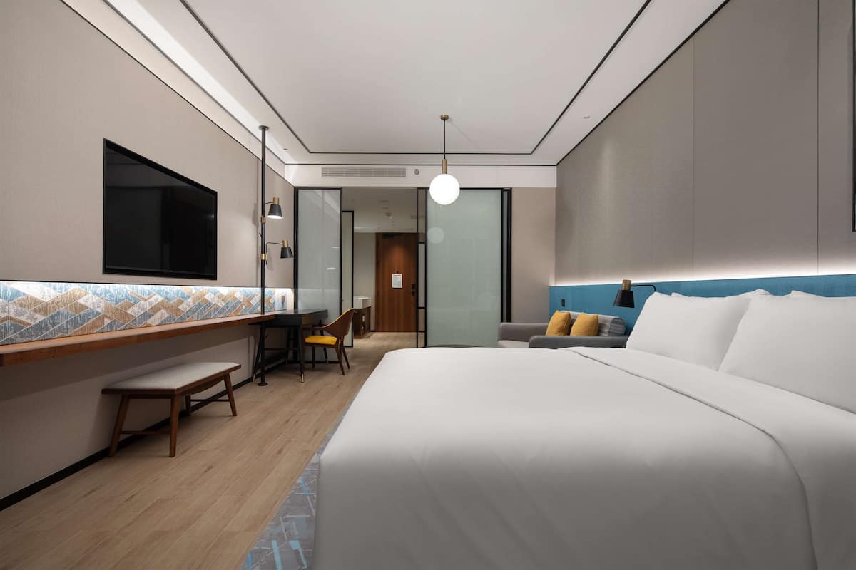 Una habitación de hotel moderna con una cama grande, un escritorio con una silla, un pequeño banco y un televisor en la pared.