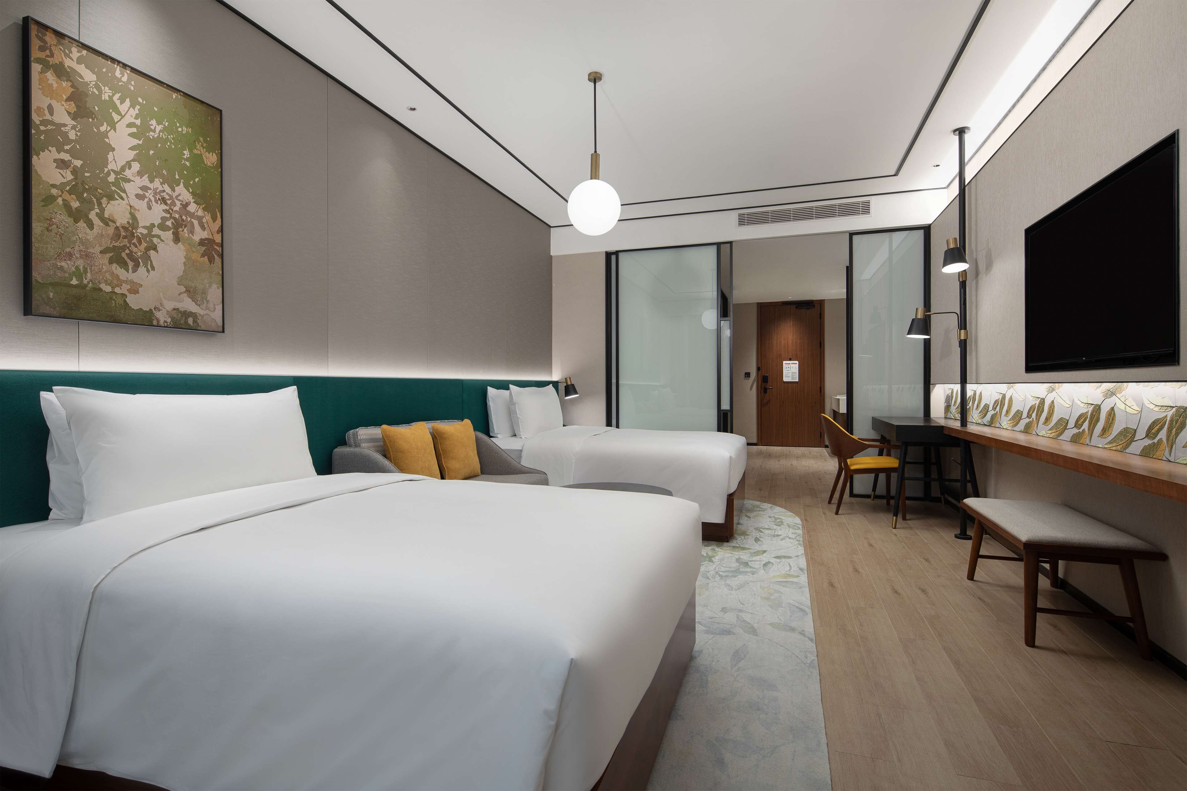 Quarto de hotel moderno com duas camas, uma escrivaninha e uma televisão.