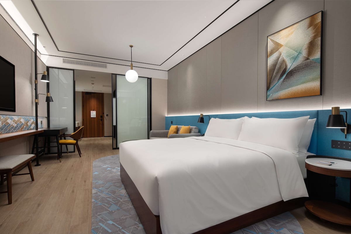 Una habitación de hotel moderna con una cama grande, un escritorio con una silla, una mesita pequeña y un televisor instalado en la pared.