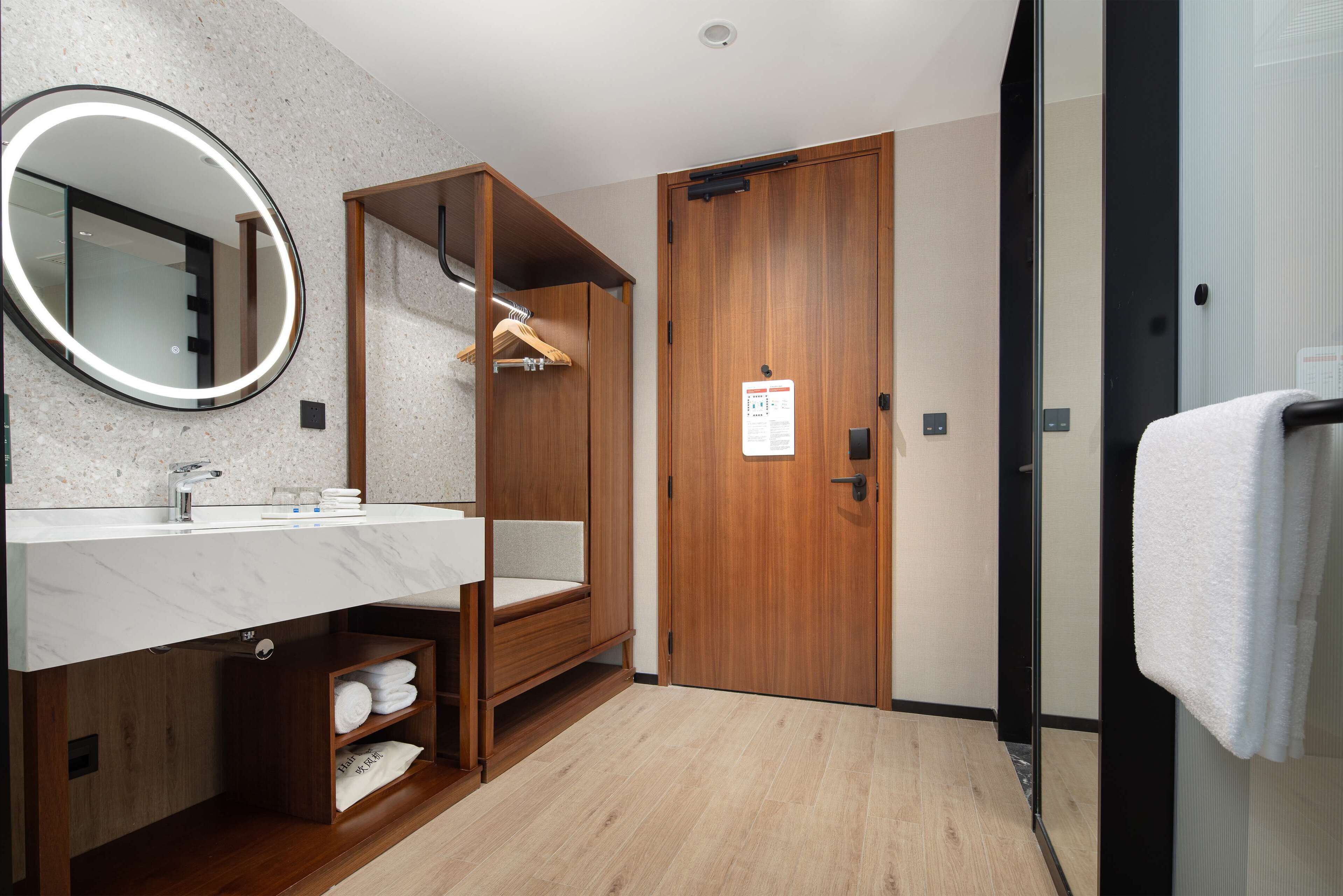 A modern bathroom with a marble sink, wooden vanity, and a large mirror with built-in lighting.