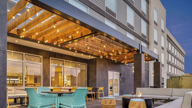 Un espace extérieur aménagé avec des tables et des chaises, un foyer et une terrasse couverte décorée de guirlandes lumineuses.