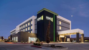 Un hôtel moderne, reconnaissable à son grand panneau « Home 2 », doté d’un parking couvert et d’une entrée agrémentée d’un aménagement paysager.