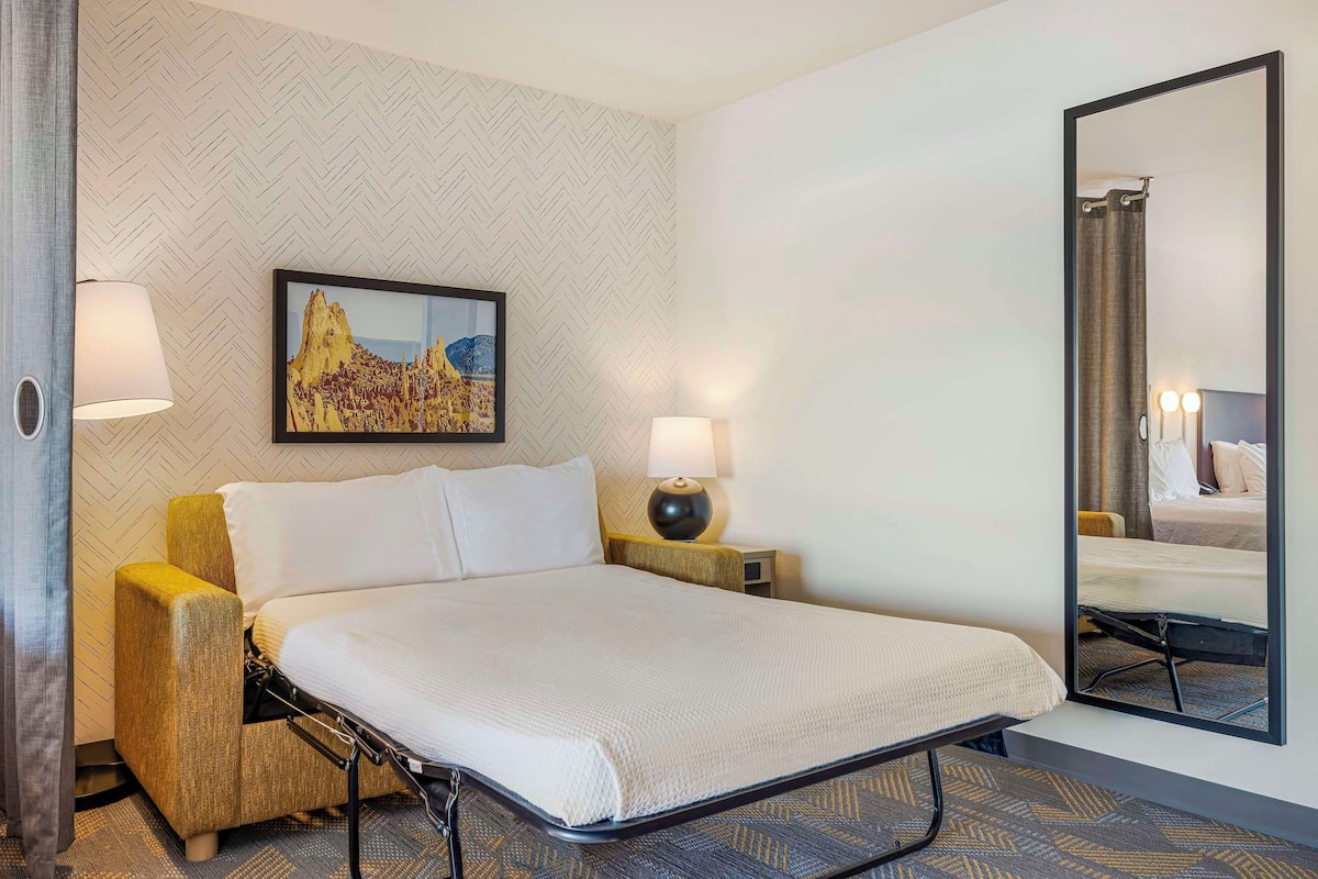 Une chambre d’hôtel avec un lit, deux lampes de chevet, un grand miroir et un mur orné d’un motif en chevrons.